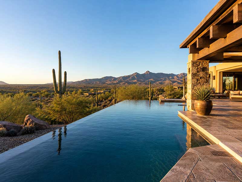 Infinity pool at a Tucson-area desert home overlooking saguaro cacti, desert landscaping, and distant mountain views.